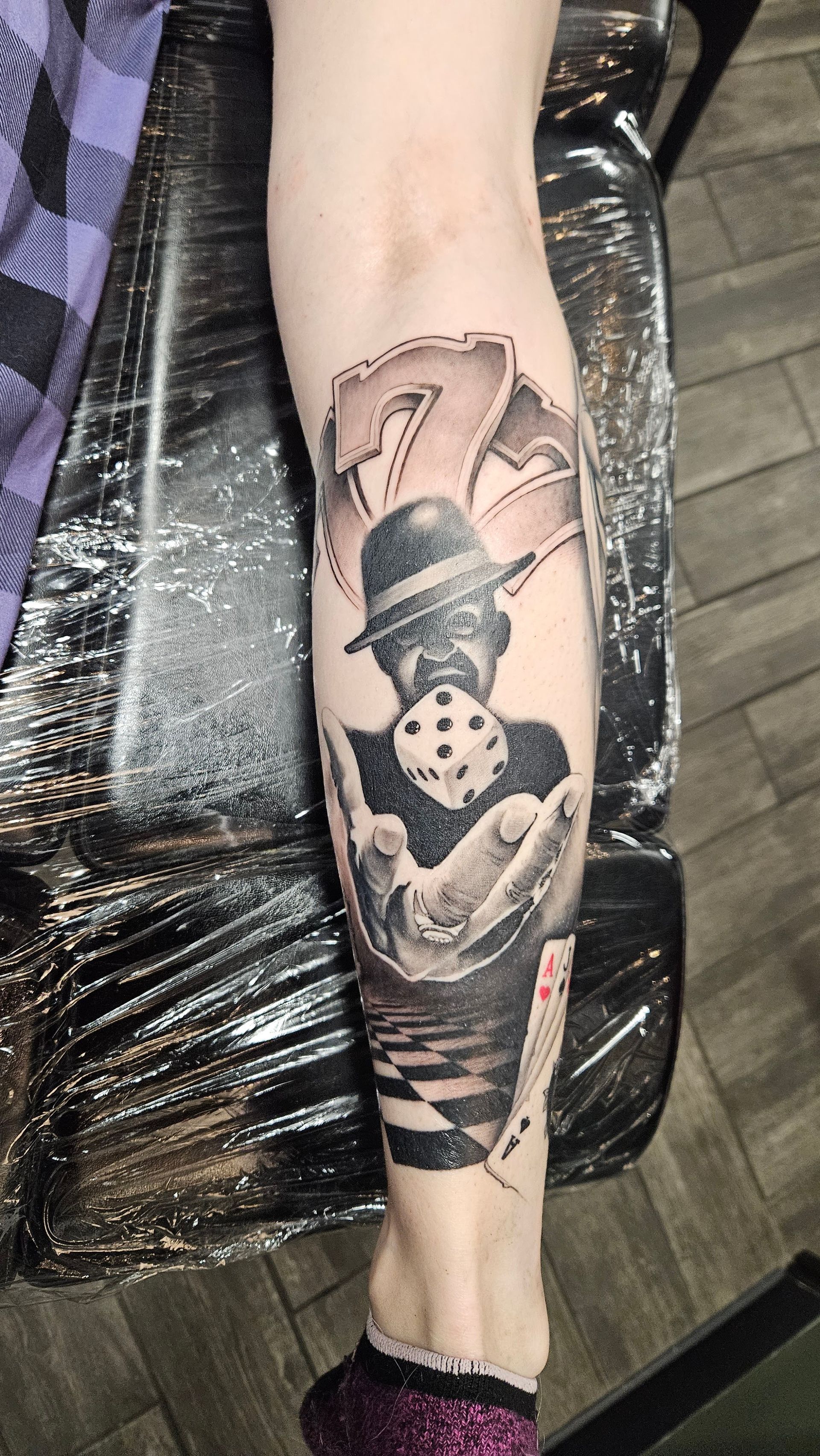 Black-and-gray tattoo of a masked figure on a forearm, with bold shapes and shading