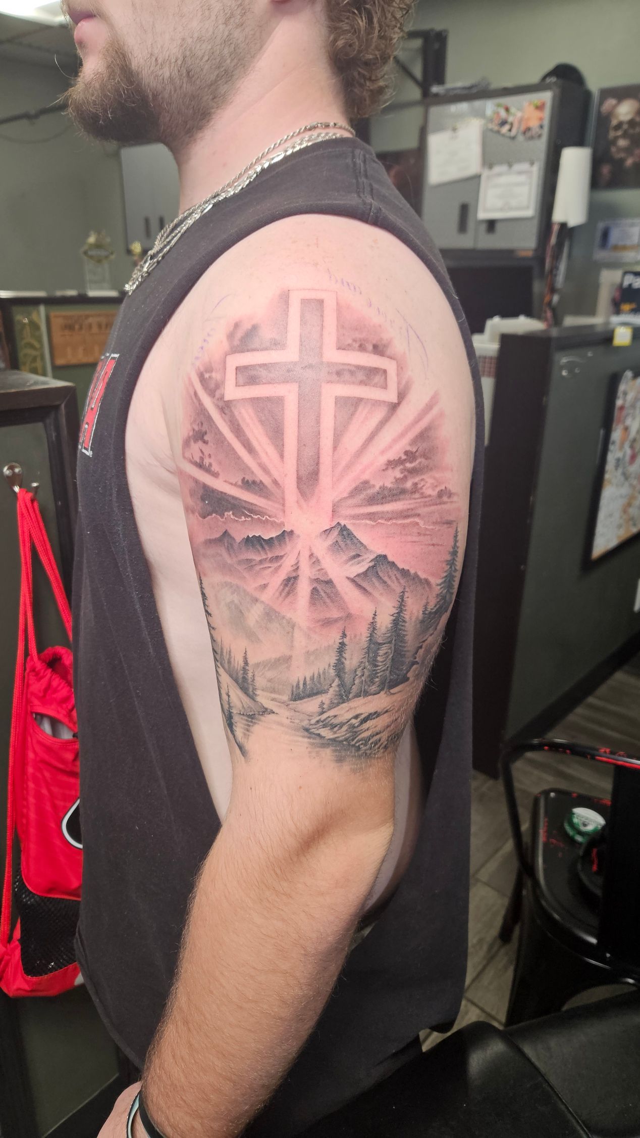 Side-view of a person in a black sleeveless shirt showing a large pink cross tattoo on the upper arm