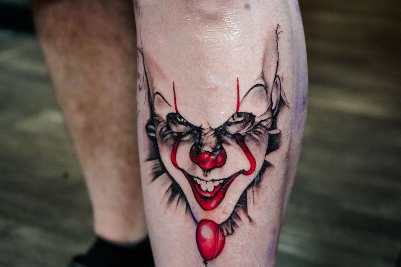 A close up of a tattoo of a clown on a person 's leg.