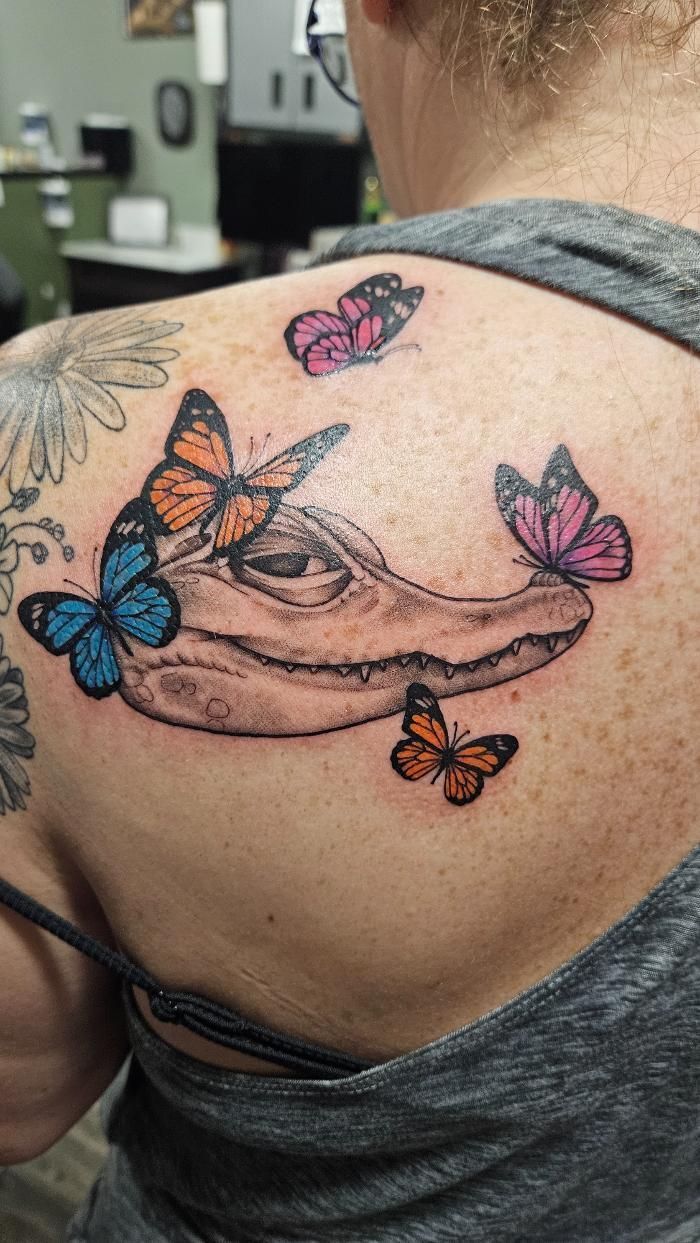 A woman has a tattoo of a crocodile skull with butterflies on her back.