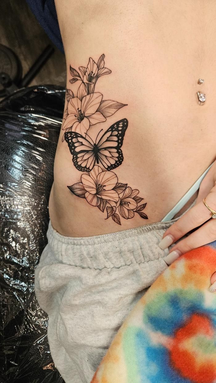 A woman has a tattoo of butterflies and flowers on her side.