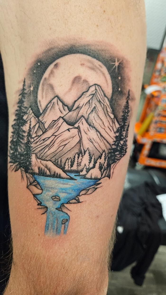 A man has a tattoo of mountains and a river on his arm.