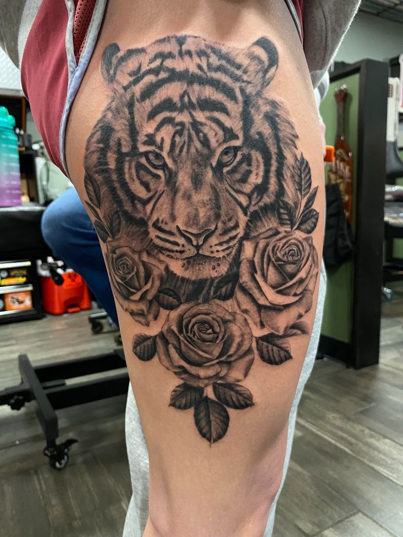 A person has a tattoo of a tiger and roses on their leg.