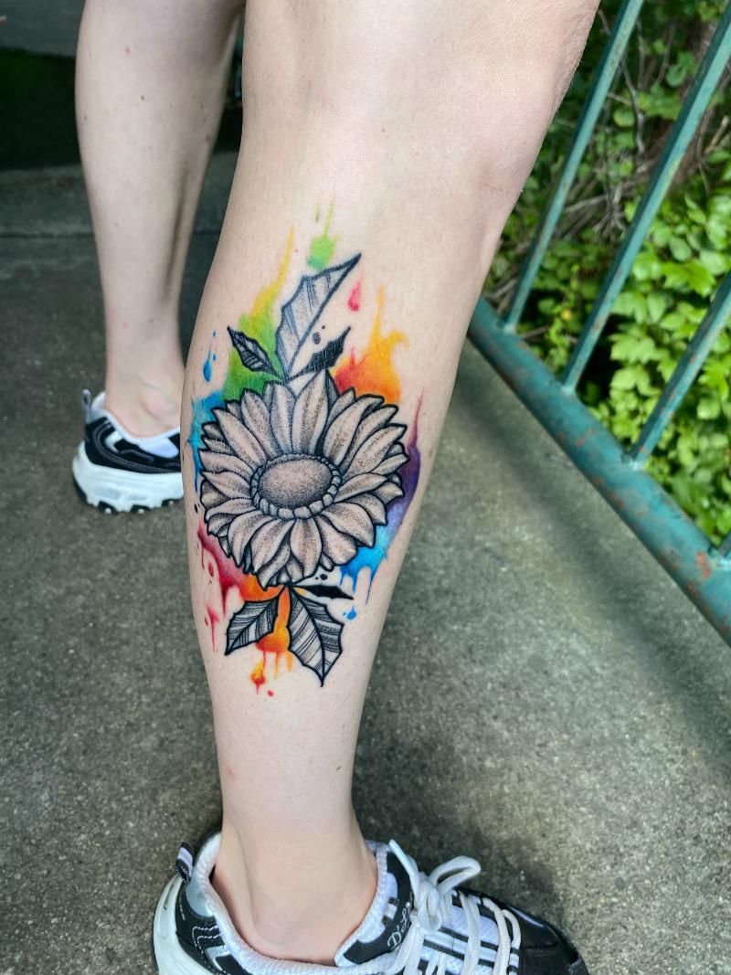 A person has a colorful tattoo of a sunflower on their leg.