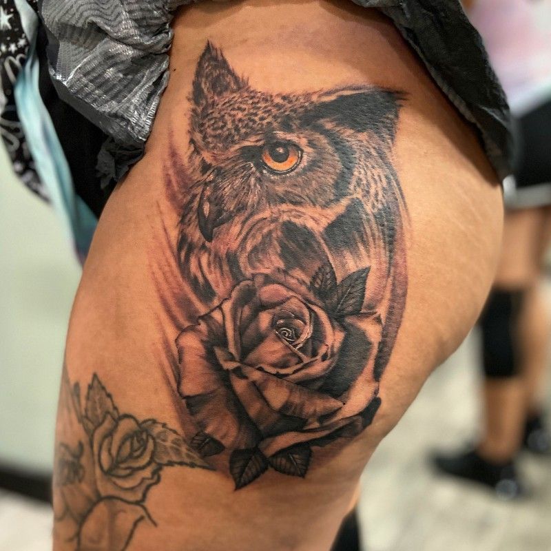 A woman has a tattoo of an owl and a rose on her thigh