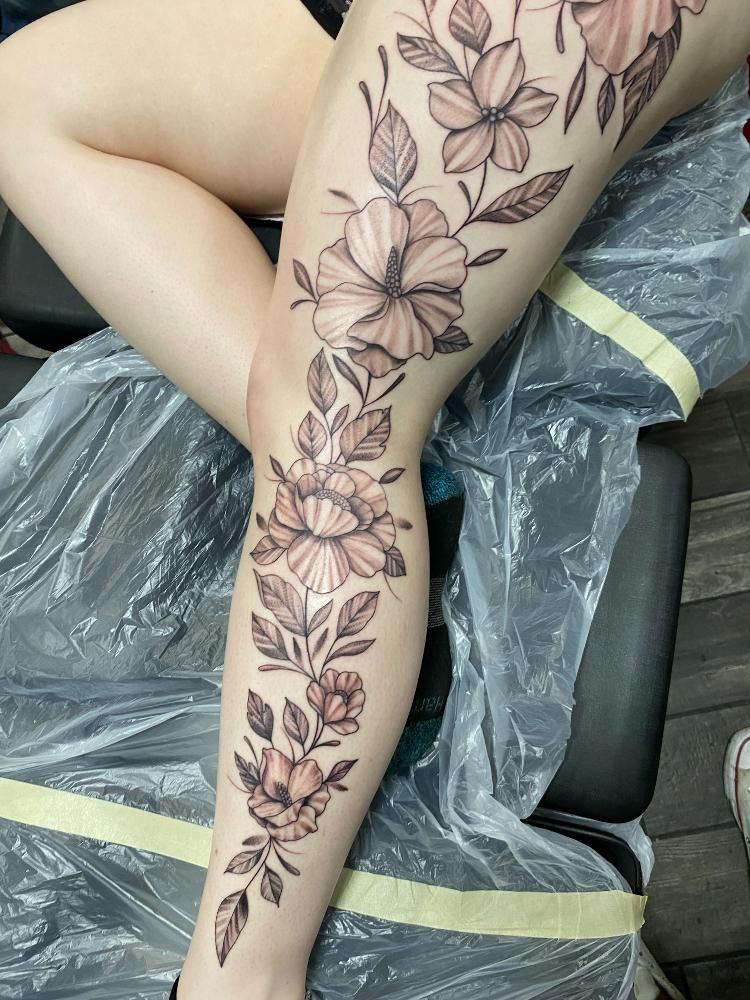 A woman has a tattoo of flowers and leaves on her leg.