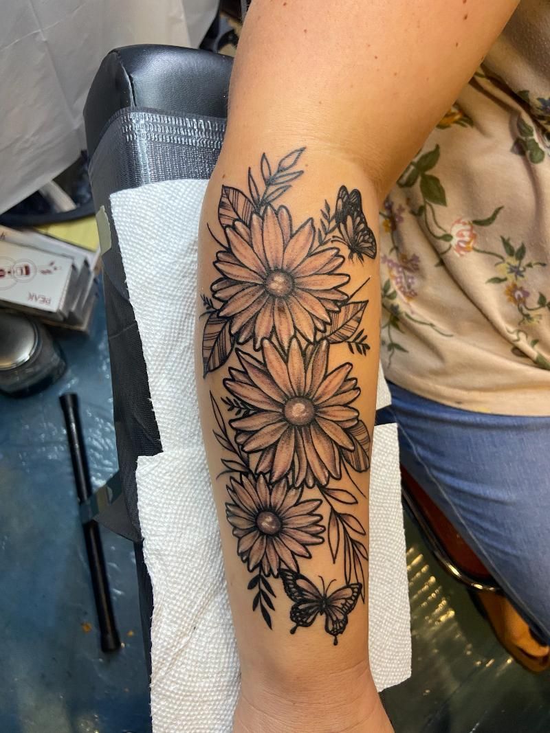 A woman has a tattoo of flowers and butterflies on her forearm.