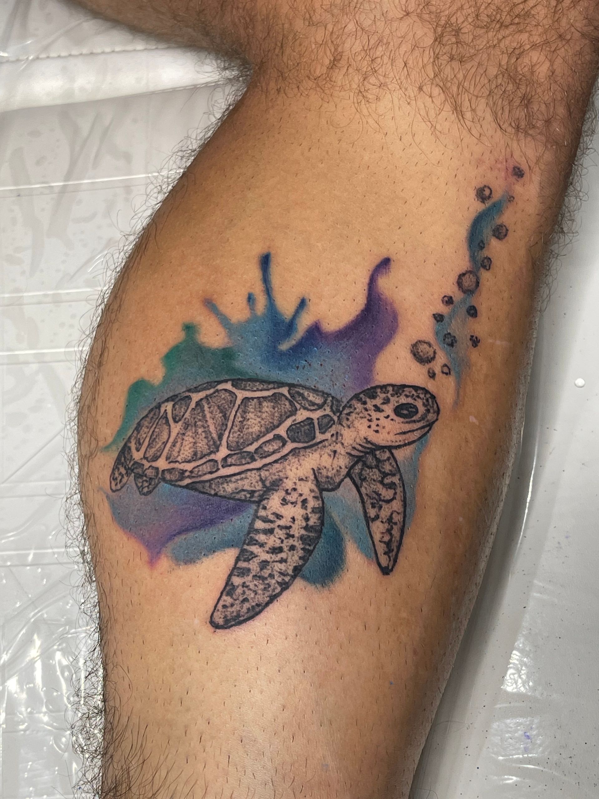 A man has a tattoo of a sea turtle on his leg.
