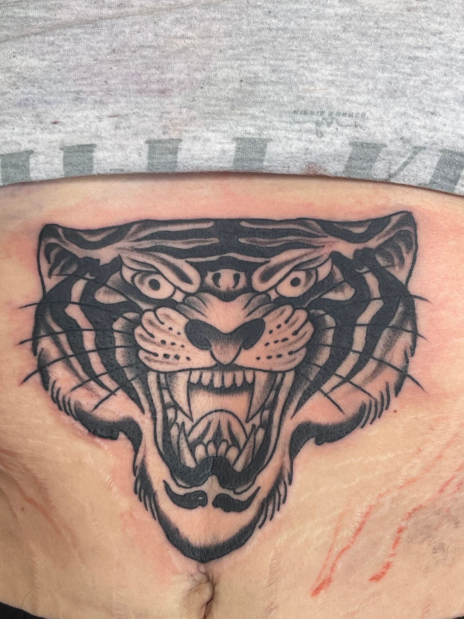 A black and white tattoo of a tiger 's head on a person 's stomach.