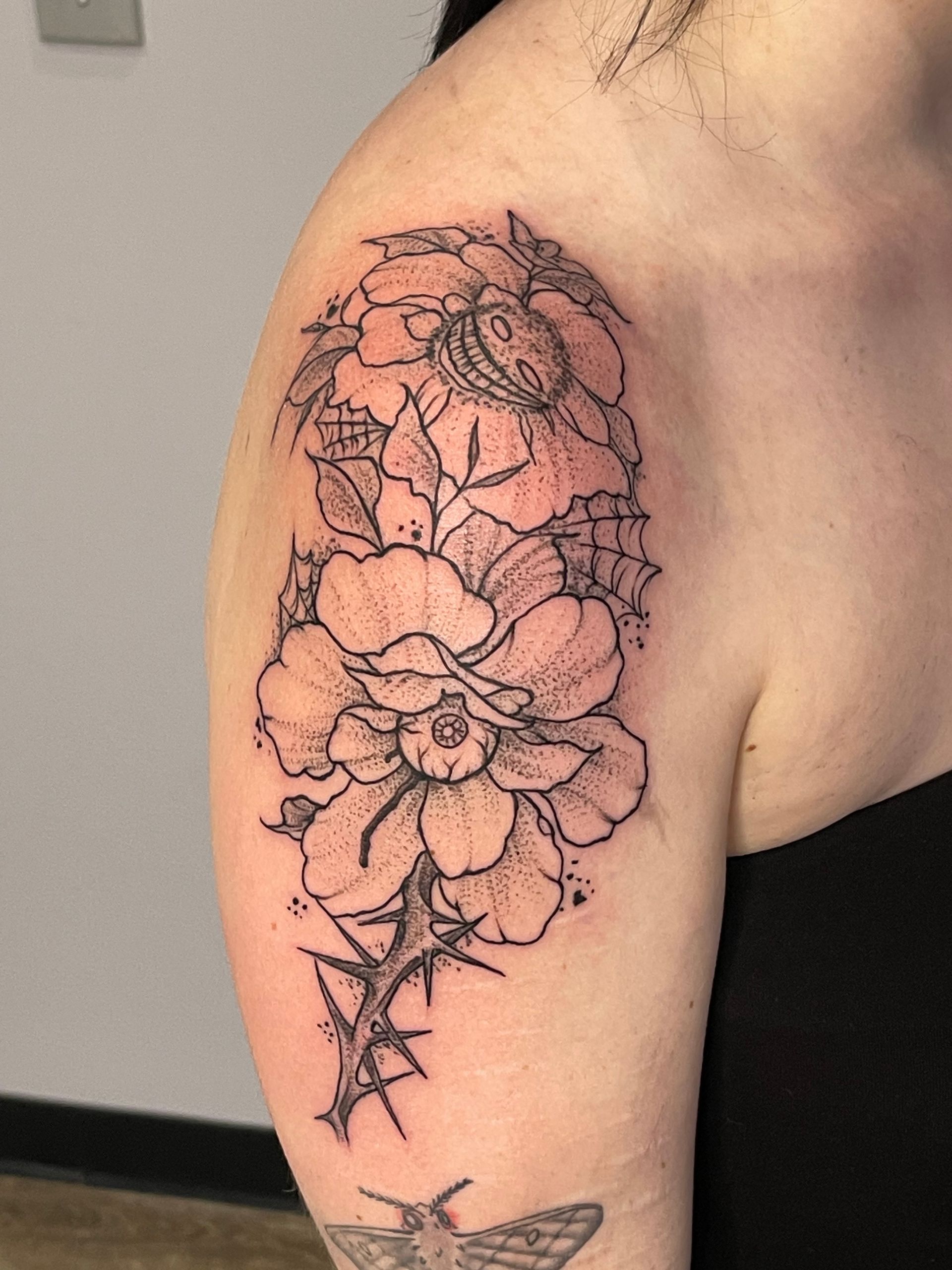 A woman has a tattoo of flowers and thorns on her arm.