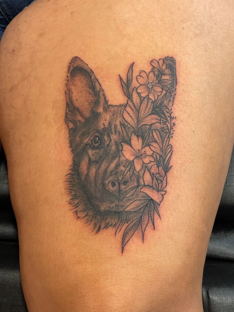 A black and white tattoo of a german shepherd surrounded by flowers on a person 's back.