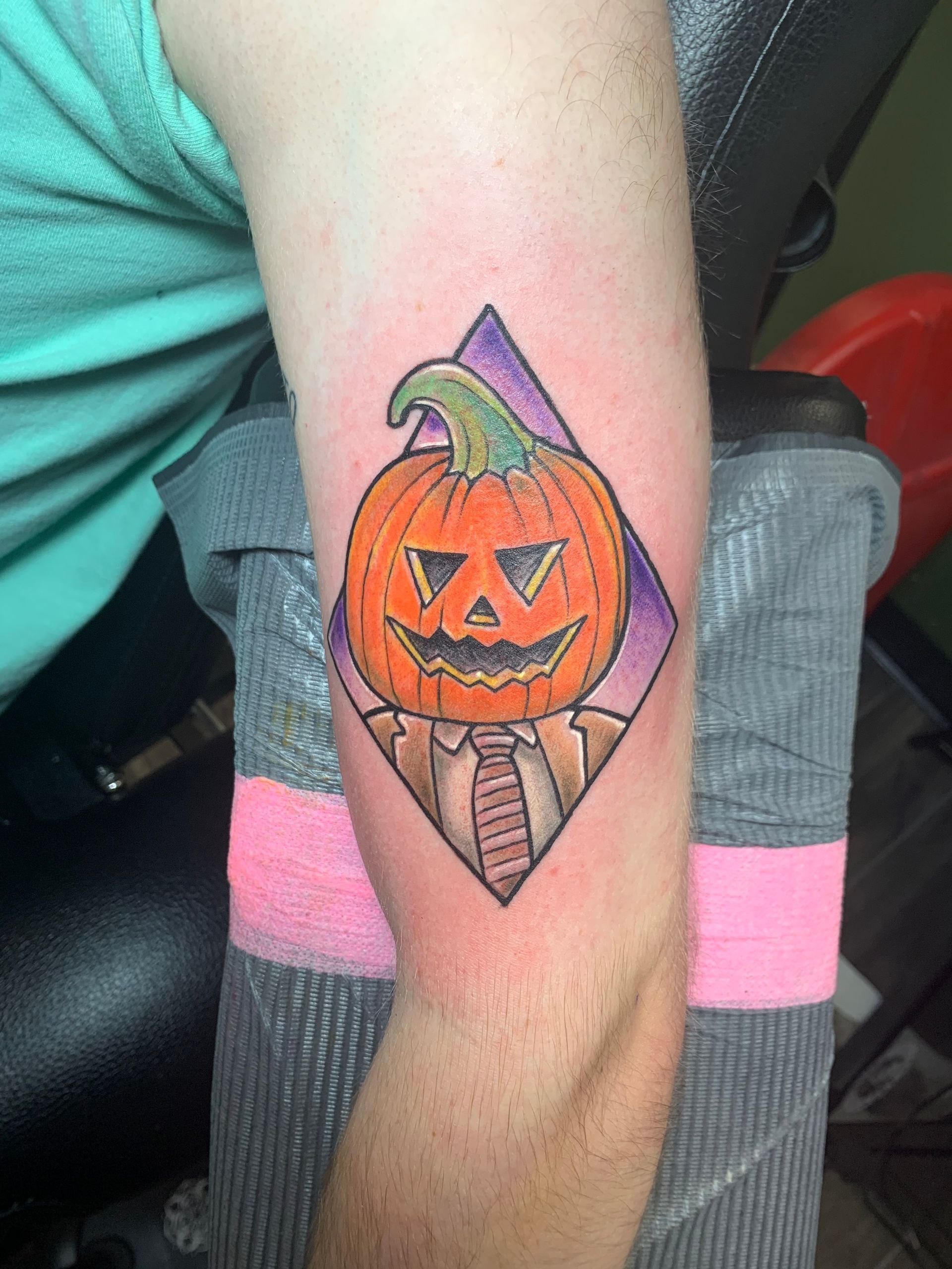 A man has a tattoo of a pumpkin with a tie on his arm.