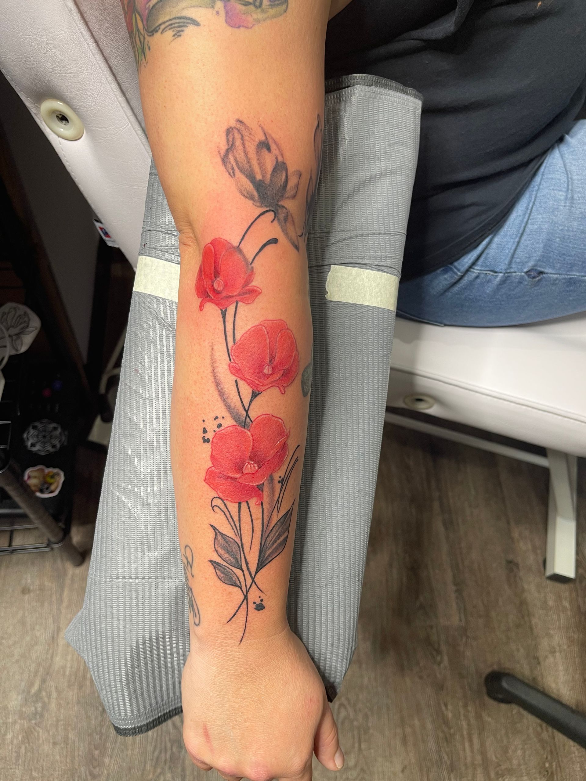 A woman has a tattoo of red flowers on her forearm.