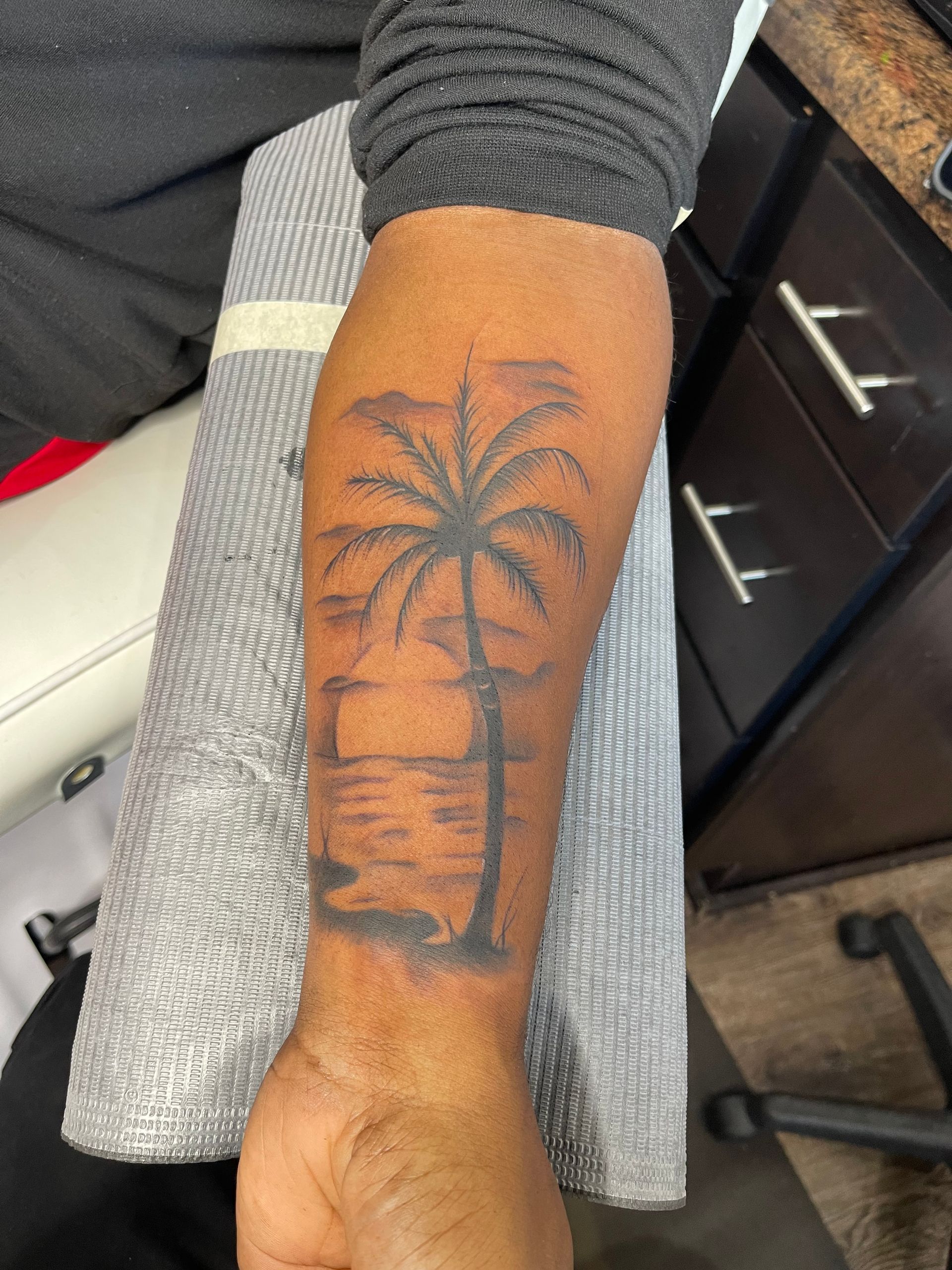 A man has a tattoo of a palm tree on his forearm