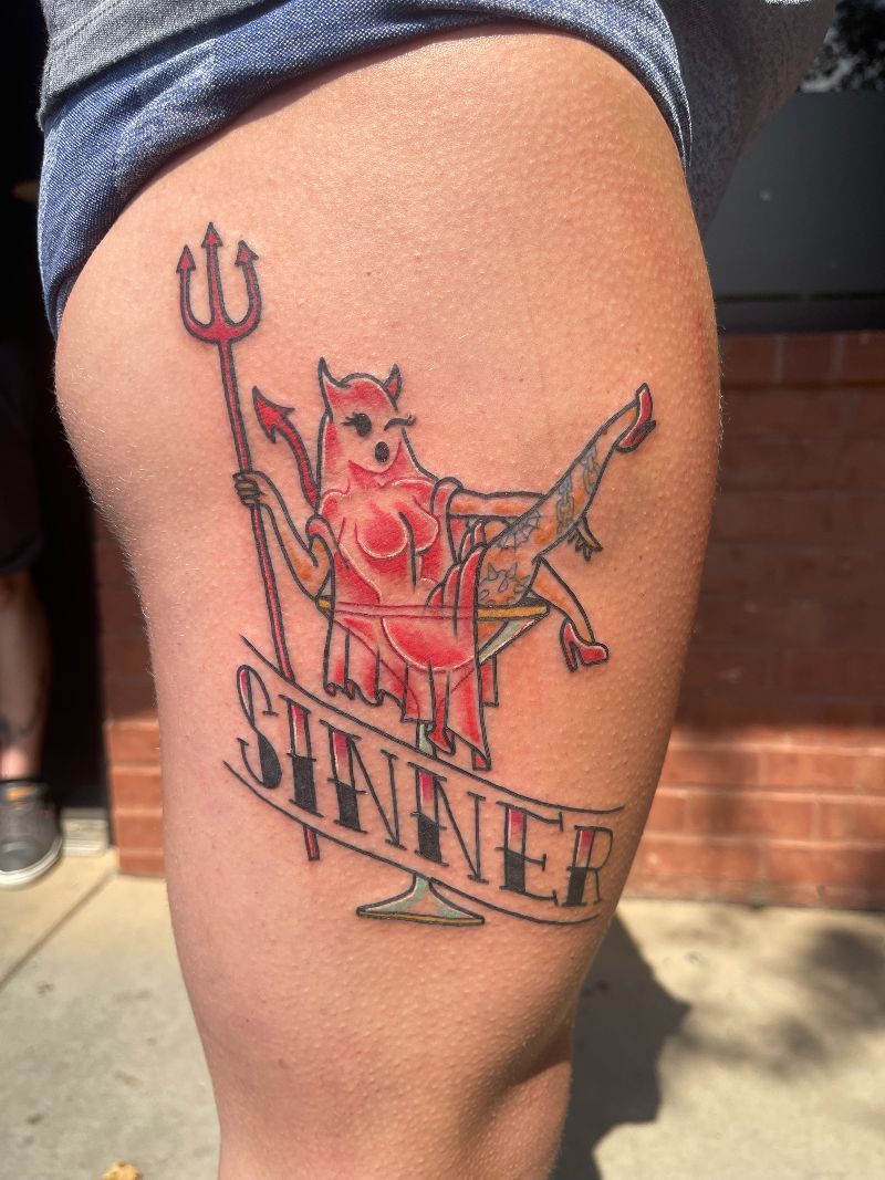 A woman has a tattoo of a devil with a trident on her thigh.
