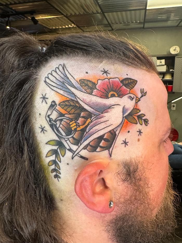 A man has a tattoo of a bird and flowers on his head.