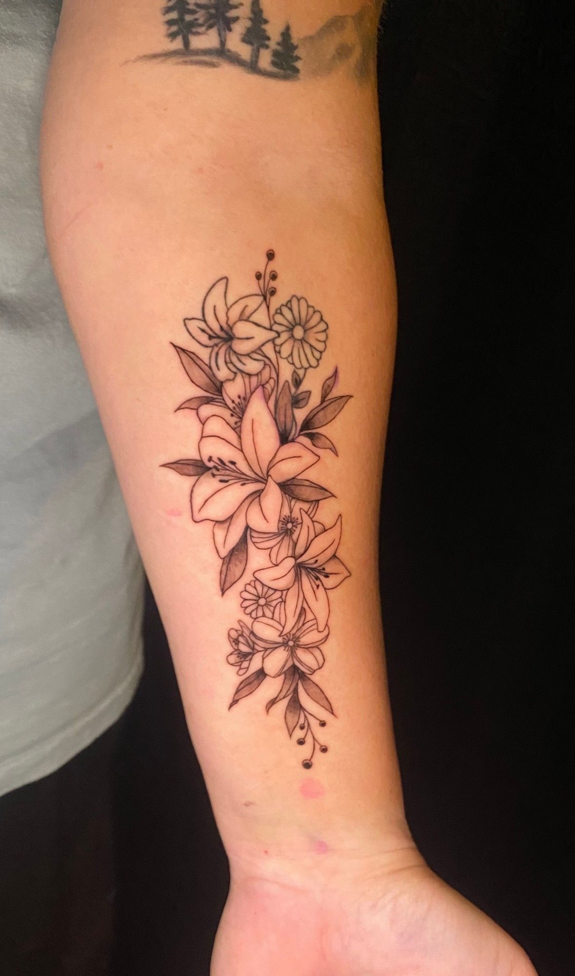 Floral tattoo on forearm with lilies and other flowers.