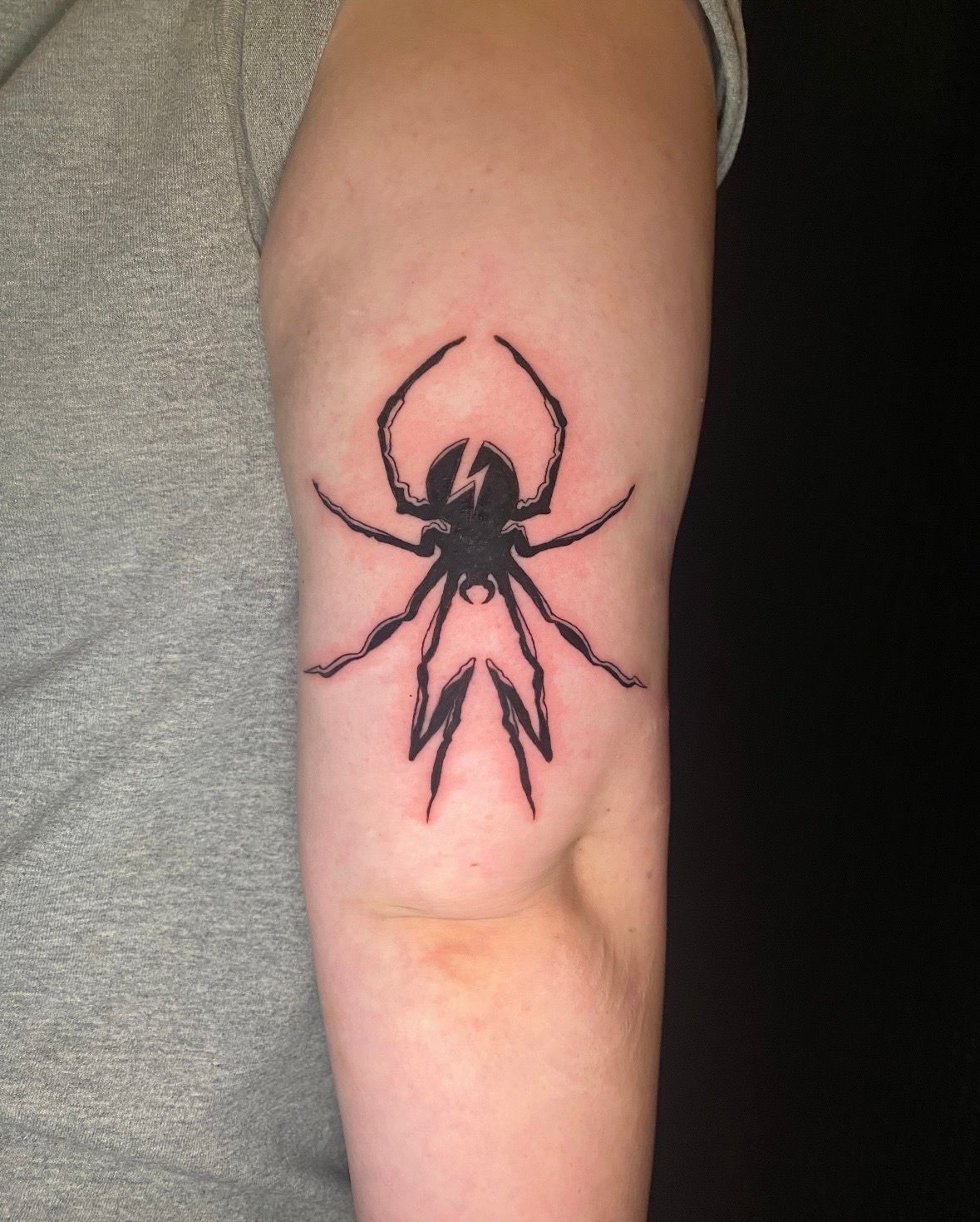 Black spider tattoo on a person's upper arm, with jagged legs.