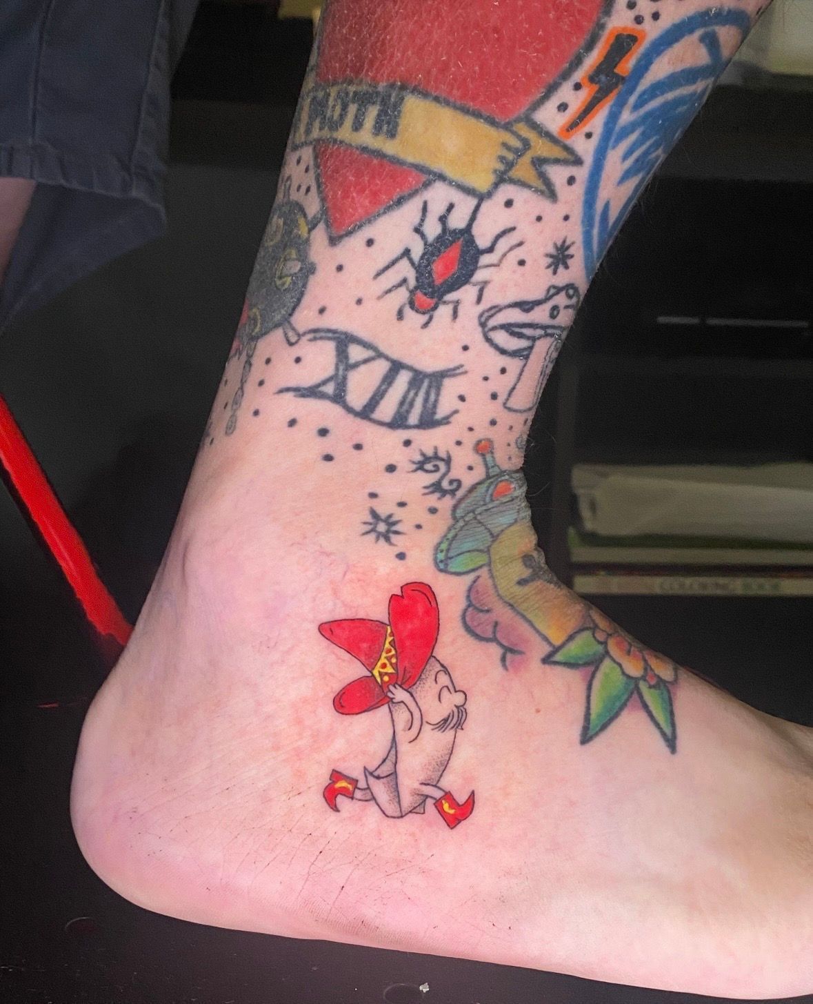 Ankle tattoo with a red hat figure running; other tattoos visible on the leg.