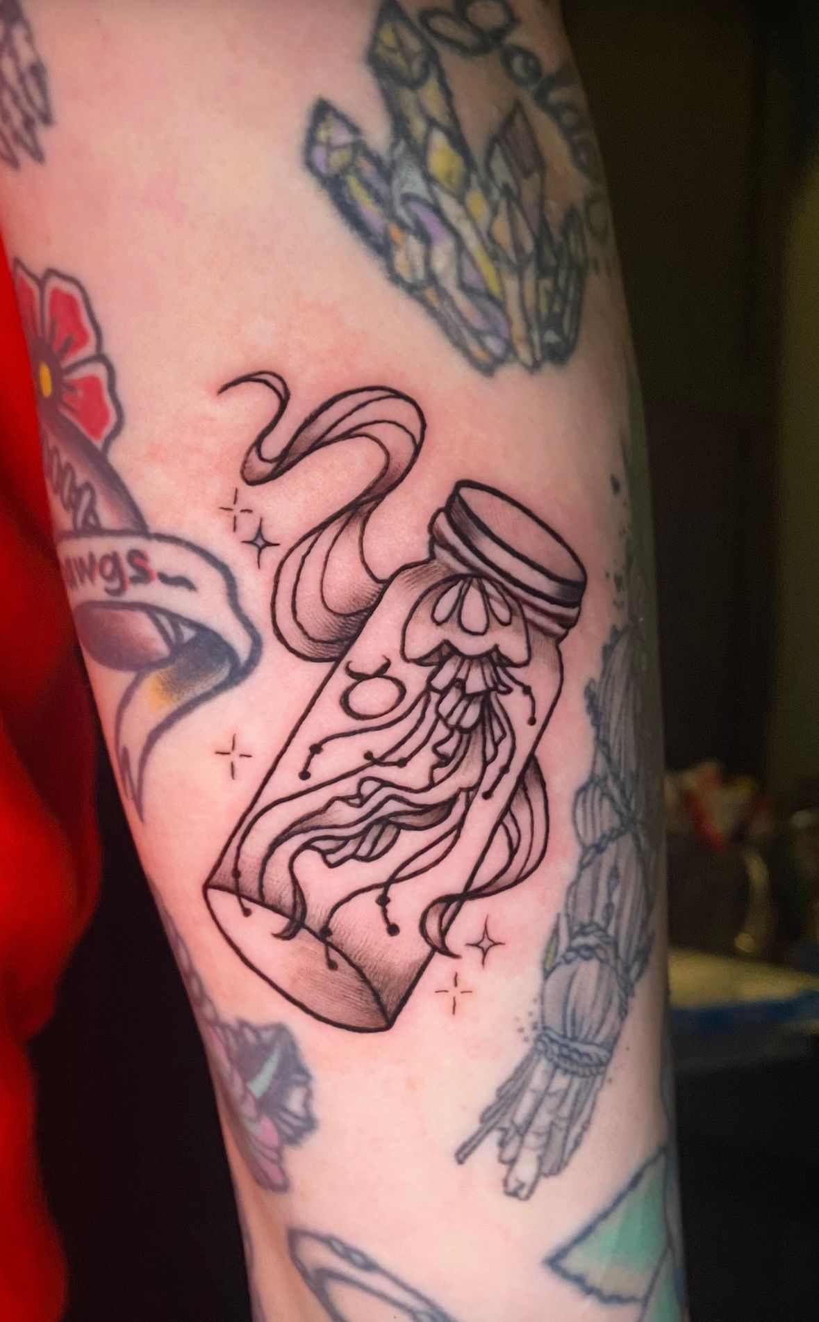 Tattoo of a jellyfish in a jar with flowing tendrils and sparkling stars.