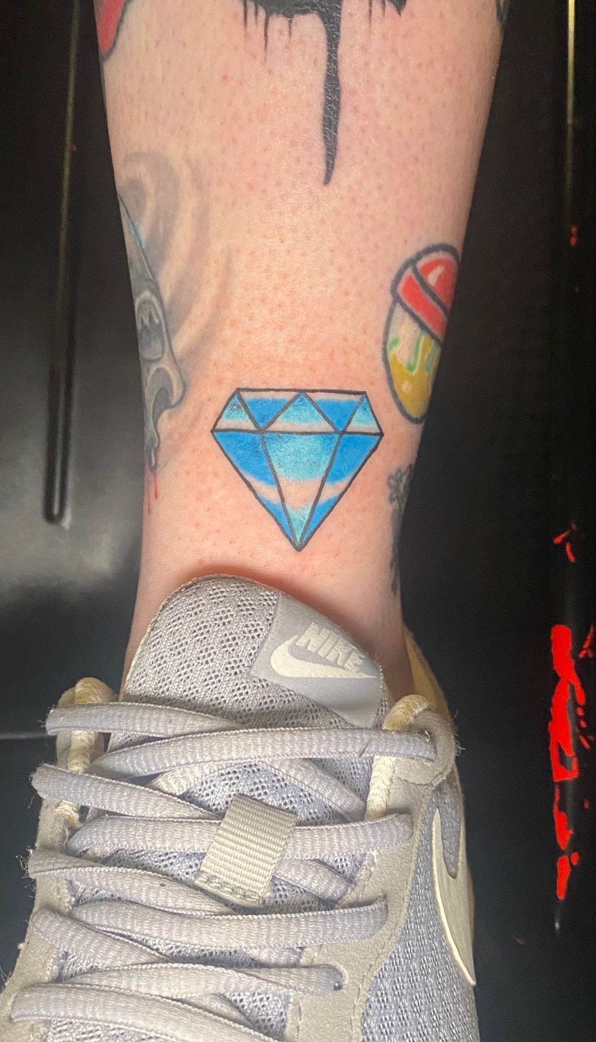 Diamond tattoo on an ankle, with a sneaker in the foreground. Blue and white colors.