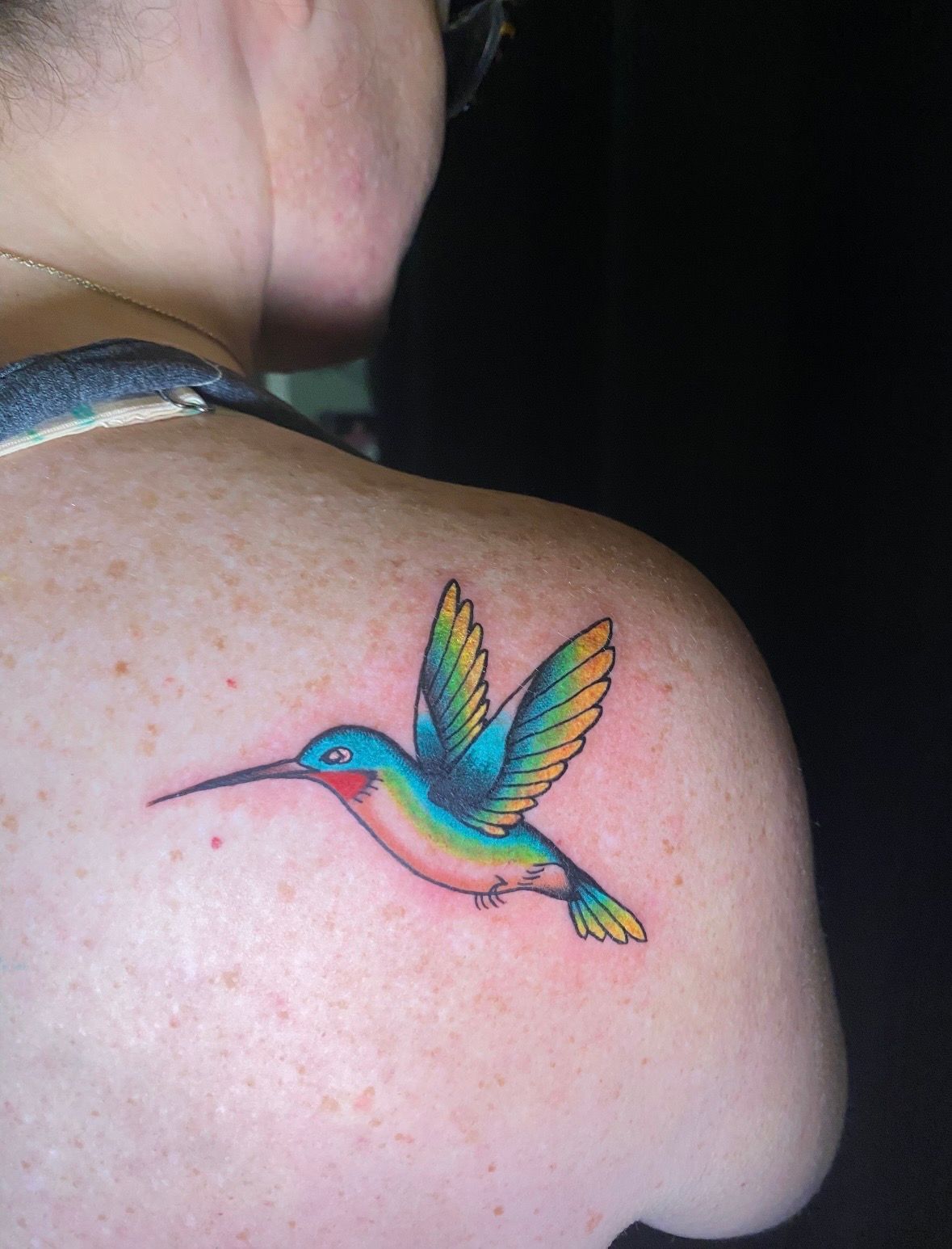 Hummingbird tattoo on shoulder, with blue, turquoise, yellow, and red colors.