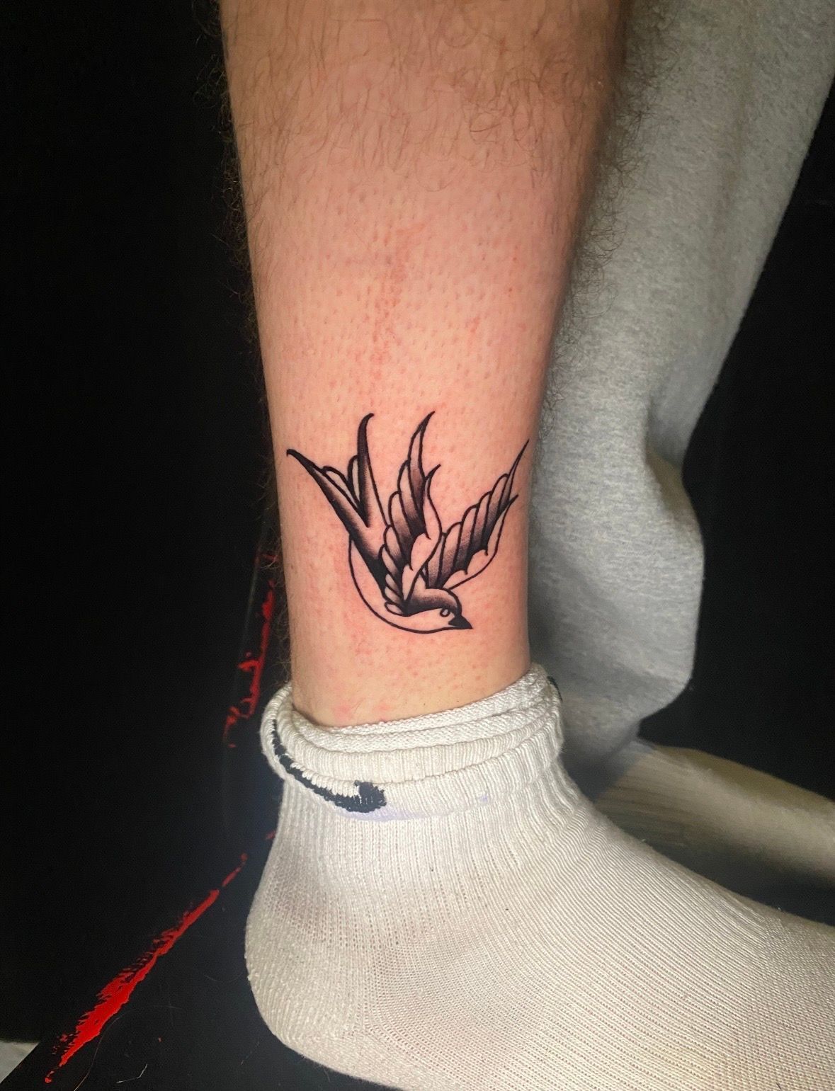 Black and white swallow tattoo on ankle above a white sock.
