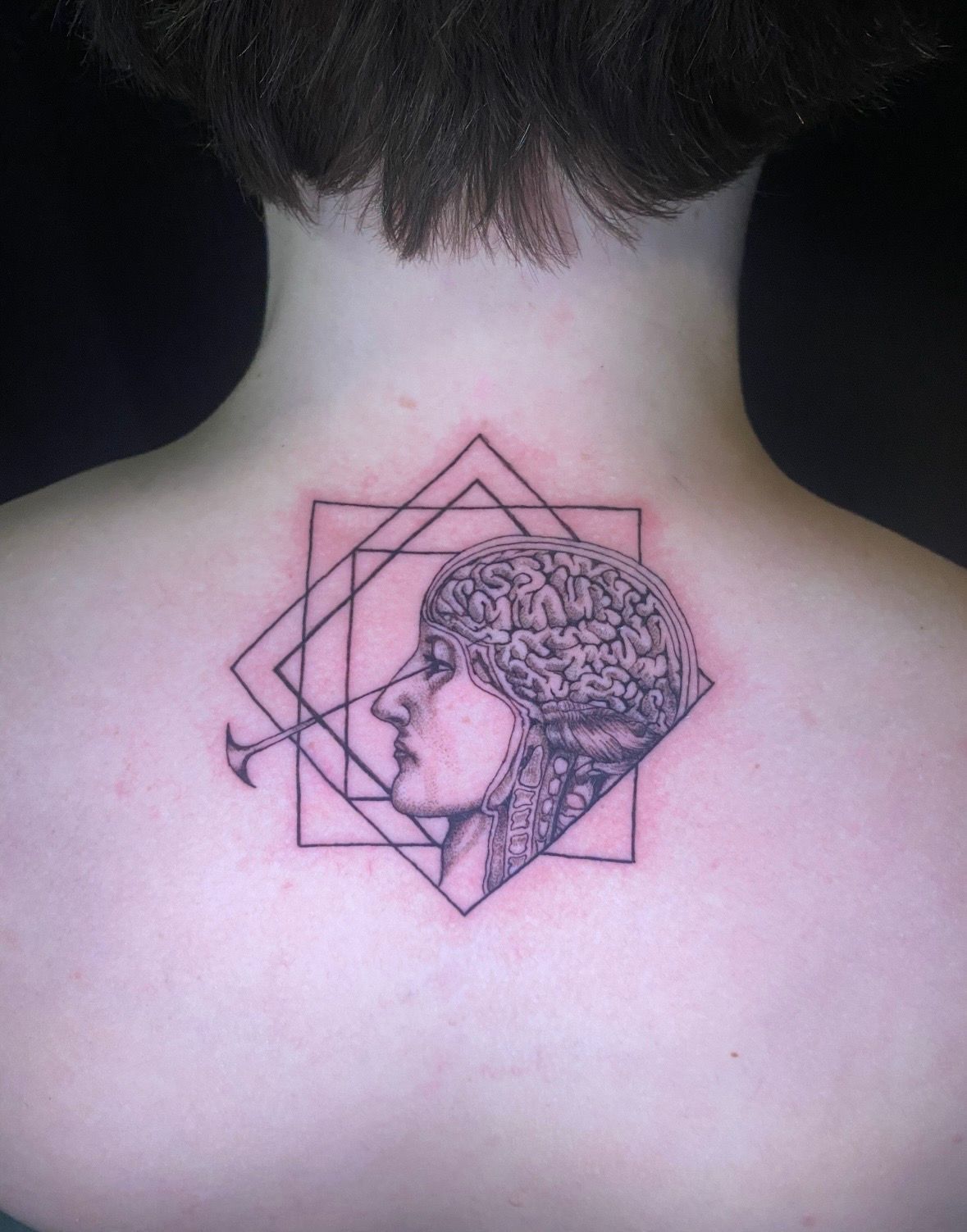 Tattoo of a person's profile within a geometric design. The person's head shows a brain detail.