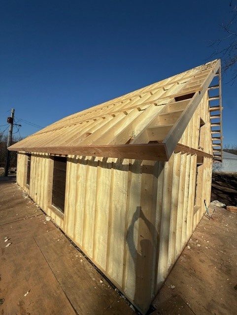 A wooden shed frame under construction stands outdoors against a clear blue sky on a sunny day.
