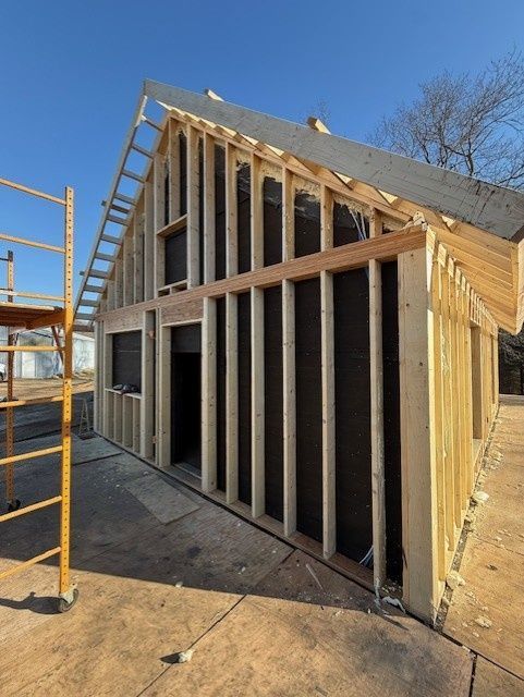 Wood framing and black weather barrier on an outdoor building structure under a clear blue sky, next to yellow scaffolding.