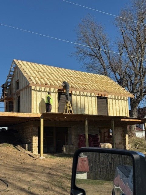 Two people stand on the framing of a house construction site under a clear blue sky.