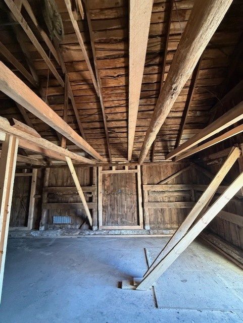 An interior view of a rustic wooden structure featuring a gabled roof, exposed support beams, and a concrete floor.