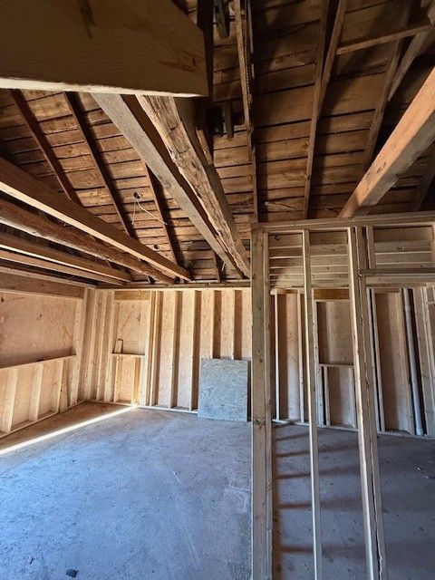Unfinished attic room with exposed wooden beams and framing, bare insulation, and a small window