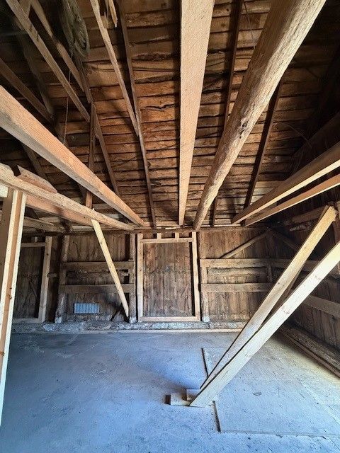 Interior of old wooden barn with exposed beams and slanted supports over a dirt floor