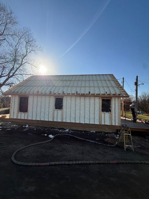 Small white house under construction with a metal roof, seen in bright sunlight on a clear day.