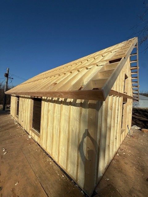 Partially built wooden house under construction on a dirt lot under a clear blue sky