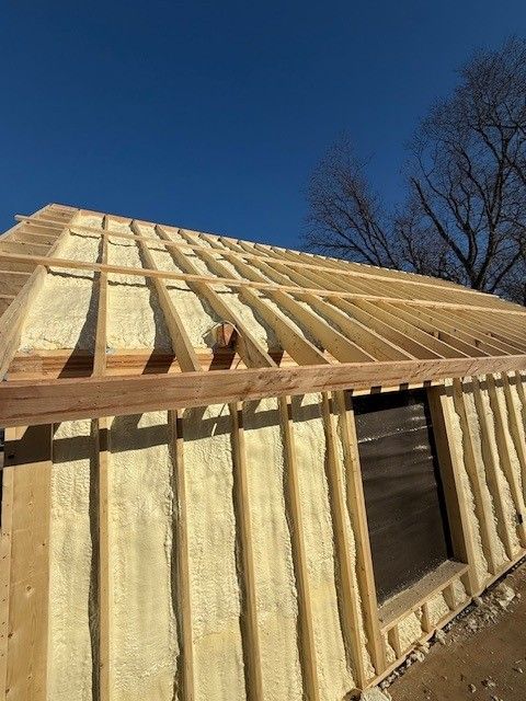 Wood-framed house under construction with exposed insulation and a large window opening under blue sky