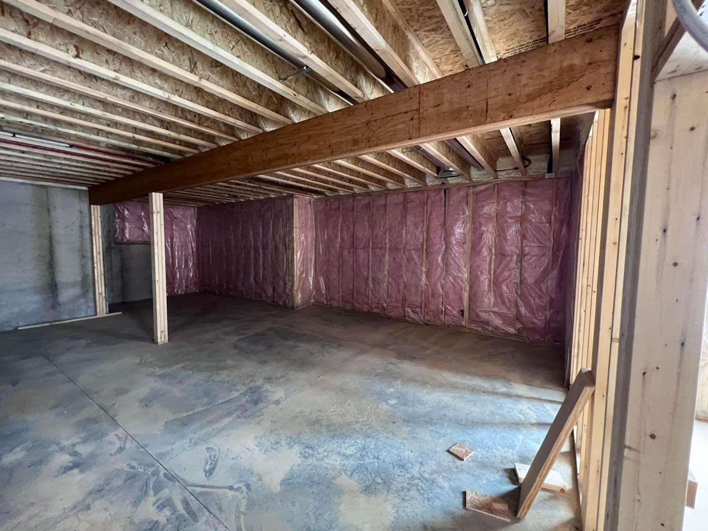A basement under construction with pink insulation and wooden beams.
