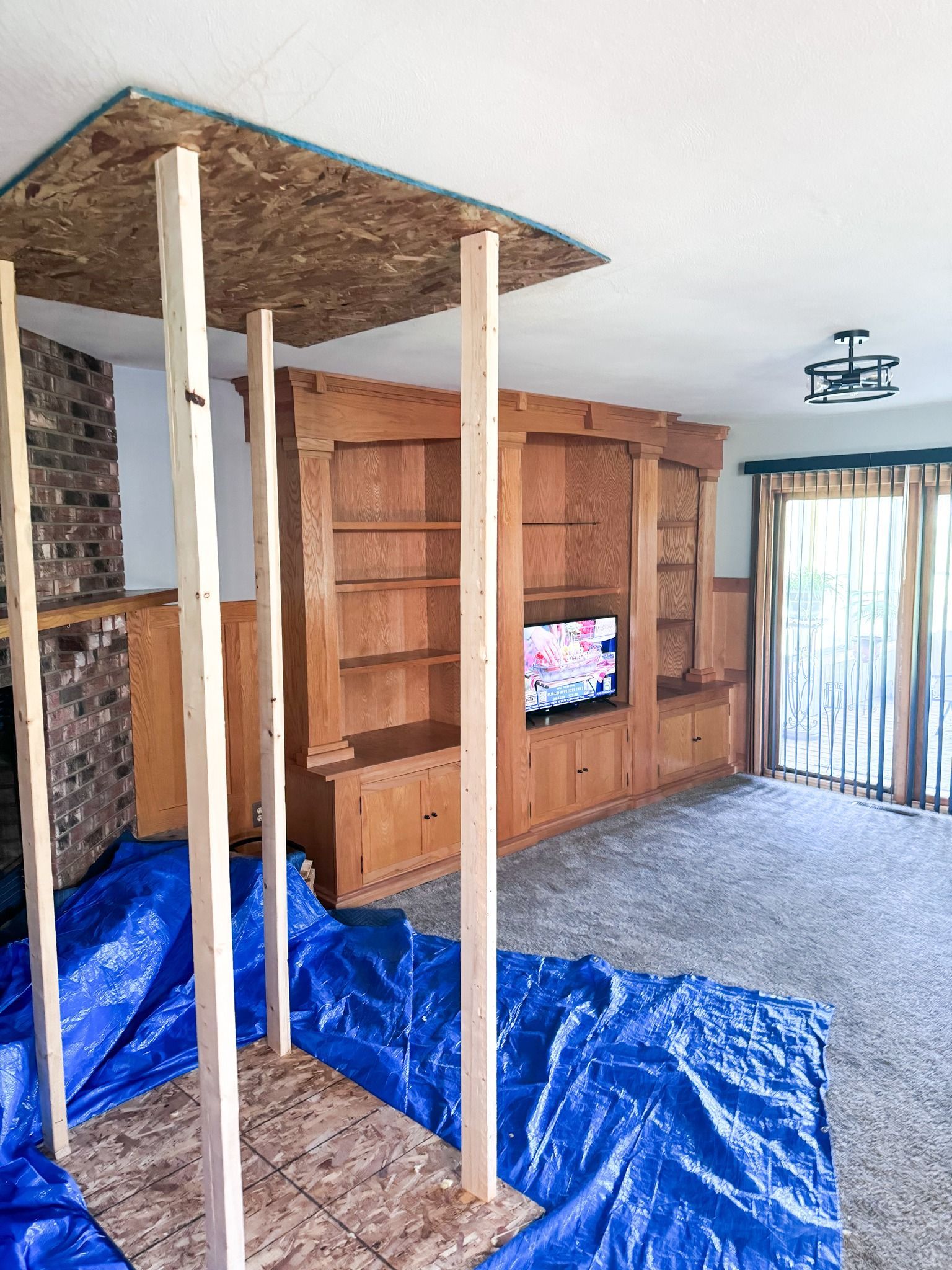 A living room is being remodeled with wooden shelves and a flat screen tv.