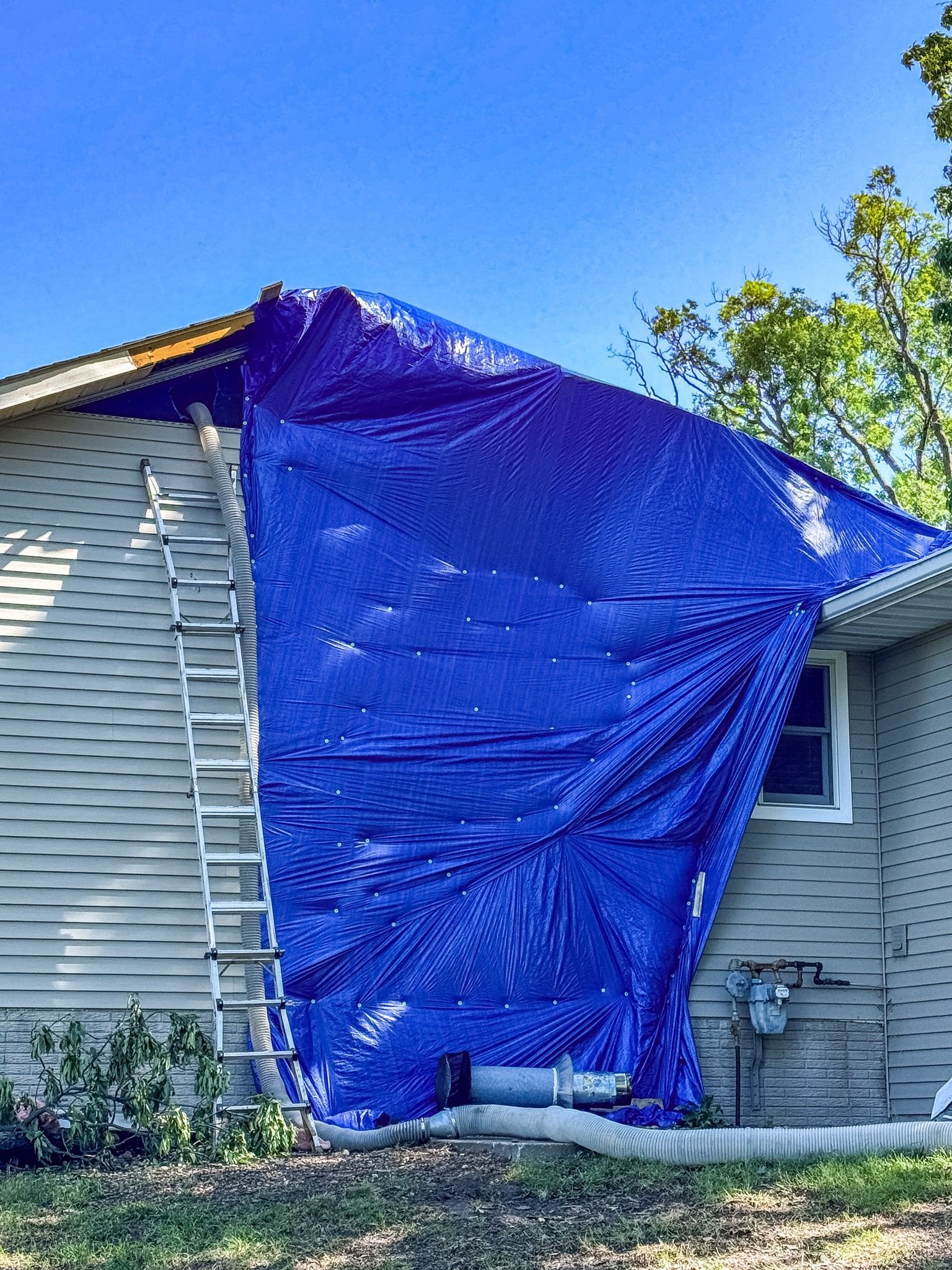 A blue tarp is covering the side of a house.
