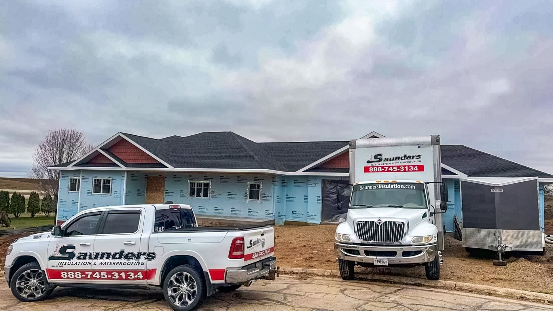 Two trucks are parked in front of a house under construction.