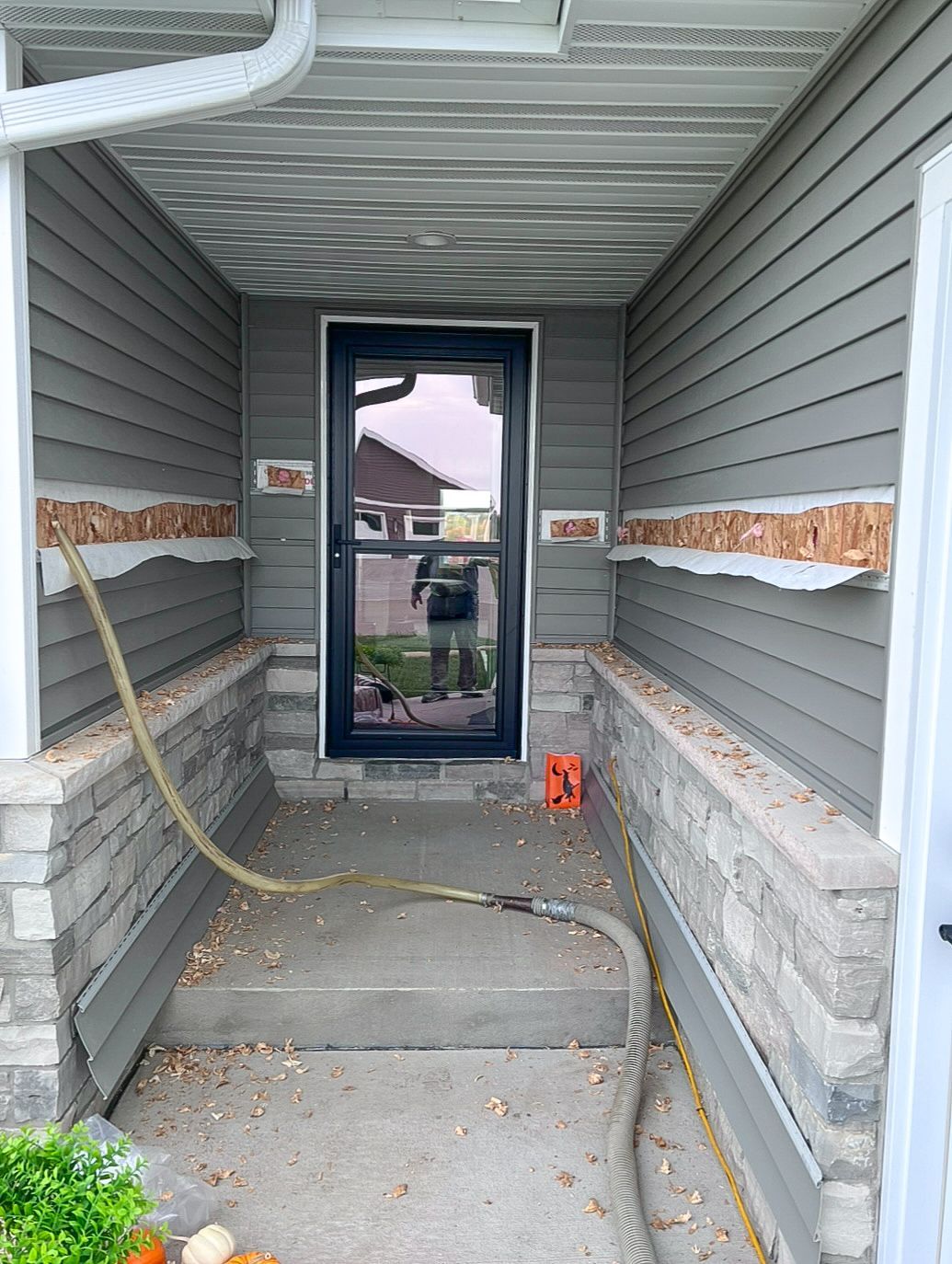 A porch with a black door and a hose attached to it.