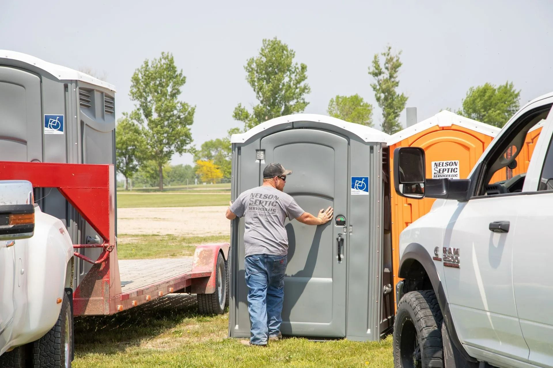 Man near portable toilets being unloaded from a trailer, a white truck parked next to it.
