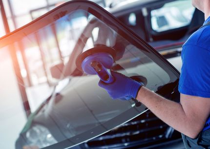 Person polishing a car windshield with a suction tool in a garage