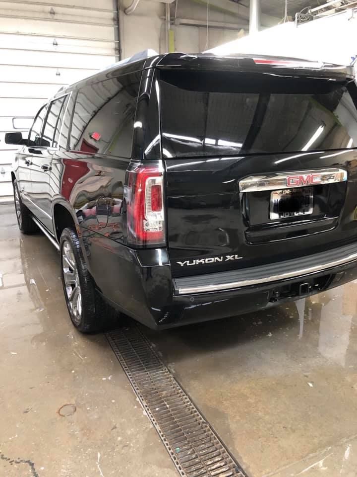 The back of a black gmc yukon is parked in a garage.