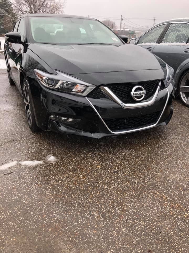 A black nissan maxima is parked in a parking lot.