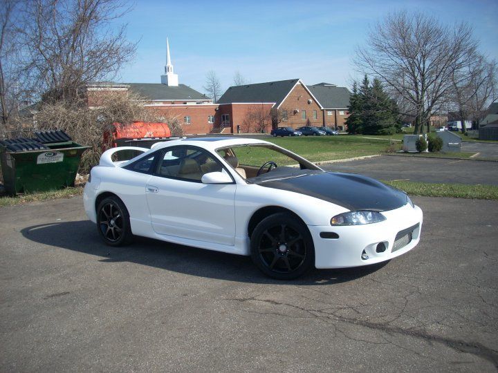 A white car with a black hood is parked in a parking lot