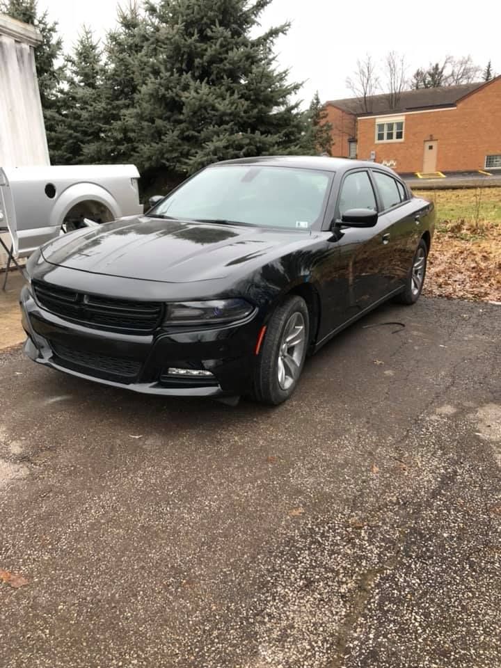 A black dodge charger is parked in a driveway next to a trailer.