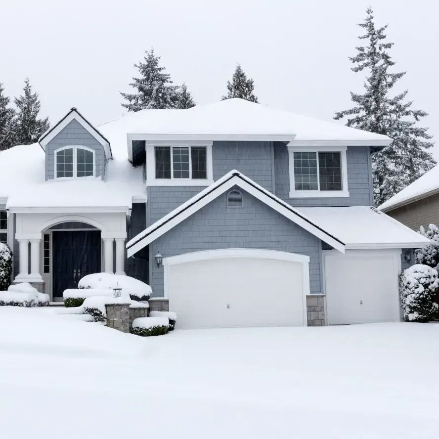 A blue house with a white garage door is covered in snow.