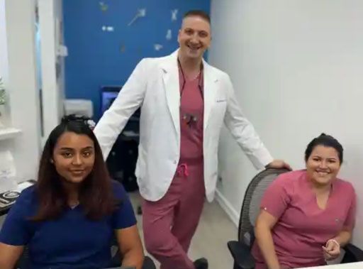 Three dental office staff smiling: a man in pink scrubs, two women in blue and pink scrubs.